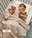 A sleeping toddler in a wooden cot, wearing a patterned sleep suit bag while cuddling two plush stuffed animals on a toddler pillow.
