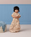 A toddler standing while wearing a tan short-sleeved Sleep Suit Bag in sleeping bag mode.