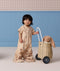 A toddler standing next to a toy cart wearing a tan short-sleeved convertible sleep suit bag in suit mode.