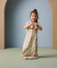 A toddler stands while holding toy binoculars and is wearing a 1.0 TOG sleep suit bag with a safari animal print.
