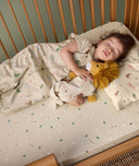 A toddler is peacefully asleep on a low-profile pillow with a safari-themed pillowcase. She is wearing a matching sleep suit bag and holding a plush lion.