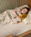A young child is peacefully sleeping in a wooden toddler bed, wearing a safari-themed sleep suit bag and cuddling a plush lion toy dressed in a matching doll-sized sleeping bag.