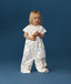 Toddler standing against a blue background wearing a white Sleep Suit Bag 1.0 TOG Daydream, featuring short sleeves and colourful all-over print