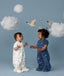 Two babies standing on a light blue background wearing 1.0 TOG Sleep Suit Bags, one in white with a colourful print and the other in blue with a moon-and-star print, reaching toward each other beneath decorative clouds and birds.