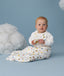 Infant sitting upright against a light blue background with decorative clouds wearing a white Sleep Suit Bag with sleeves