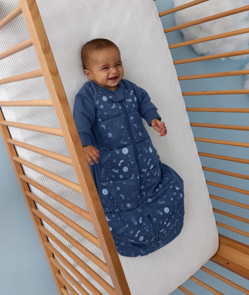Baby lying in a wooden cot wearing a blue Sleep Suit Bag 2.5 TOG.