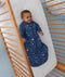 Baby lying in a wooden cot wearing a blue Sleep Suit Bag 2.5 TOG.