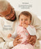 A dad holding a baby wearing a pink, patterned sleeping bag over a long-sleeved layer with text highlighting TOG rating feature and wash & wear care.