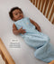 Infant lying on their back inside a wooden cot wearing a sleeveless dragonfly-patterned Sleeping Bag with text highlighting slim-fit design for  an easy transition from swaddling.