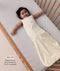 Baby lying in a wooden cot, wearing a sleeveless cream sleeping bag with text highlighting 