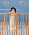 A smiling baby standing in a wooden cot wearing a cream-colored, pattern-printed sleeping bag with text highlighting 