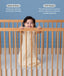 A smiling baby standing in a wooden cot wearing a cream-colored, pattern-printed sleeping bag with text highlighting 