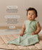 Infant sitting upright on a quilted mat, wearing a sleeveless sage green Sleeping Bag 1.0 TOG with text highlighting 