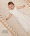 Infant lying in a wooden cot wearing a sleeveless Sleeping Bag in Oatmeal Marle with text highlighting slim fit design for easy transition from swaddling.