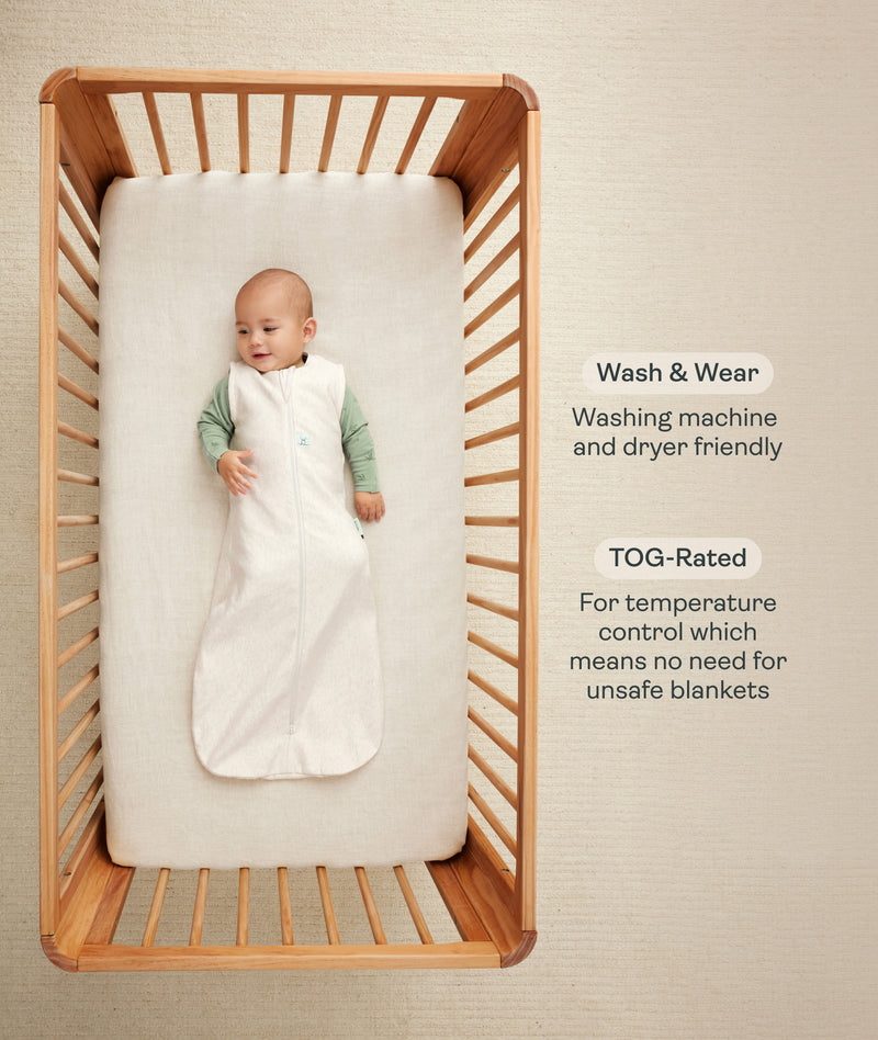 Infant wearing a sleeveless Sleeping Bag lying inside a wooden cot with text highlighting wash & wear and TOG rating features.