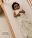 An overhead view of a smiling baby lying in a wooden cot wearing an animal-patterned Sleeping Bag, featuring a 