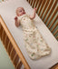 Baby lying in a cot, wearing a cream-colored sleeping bag with safari animal print