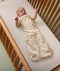 Baby lying in a cot, wearing a cream-colored sleeping bag with safari animal print