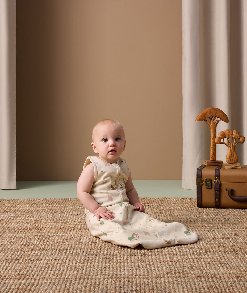 Infant sitting on a rug wearing an ergoPouch Sleeping Bag in Savannah