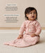 Infant sitting upright on a white rug wearing a pink long sleeve Sleeping Bag  with text highlighting organic cotton and stretchy & bell-shaped design.