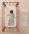 Infant lying inside a wooden cot, wearing a long-sleeve Sleeping Bag 1.0 TOG with text highlighting 