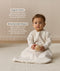 Infant sitting, wearing a sleeved Sleeping Bag 1.0 TOG Oatmeal Marle, while holding a wooden toy. Text highlighting organic cotton and stretchy-bell-shaped design.