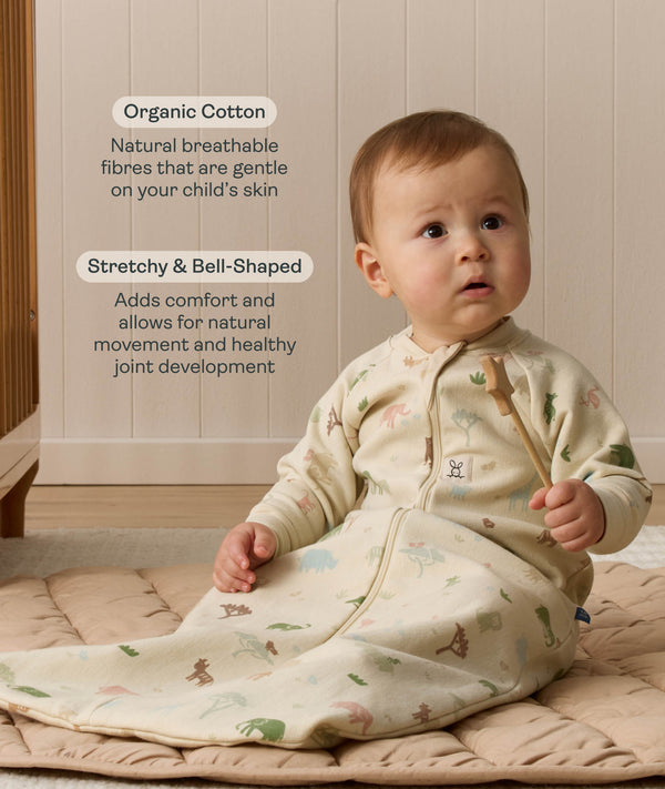 A toddler sitting on a padded mat wearing a beige safari-patterned Sleeping Bag with text highlighting organic cotton and  stretchy & bell-shaped design.