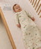 A baby wearing a slim-fit, safari-printed sleeping bag lying on a grid-patterned cot mattress, with overlay text highlighting its design.