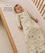 A baby wearing a slim-fit, safari-printed sleeping bag lying on a grid-patterned cot mattress, with overlay text highlighting its design.