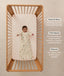 Overhead view of a baby lying on their back in a wooden cot, wearing a safari-patterned long-sleeve Sleeping Bag with text highlighting wash & wear, TOG rating, and sleeve features.