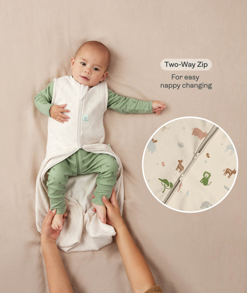 A baby lying down in a green long sleeve layer with an unzipped beige sleeping bag while adult hands hold their feet. Text highlighting 