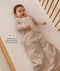 Infant lying in a wooden cot with a grid-patterned  sheet, wearing a long-sleeve Sleeping Bag 1.0 TOG with text highlighting its slim fit design for an easy transition form swaddling.