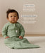 Infant sitting on a white mat, wearing a Sleeved Sleeping Bag 1.0 TOG Willow with text overlay highlighting organic cotton and stretchy & bell-shaped design.