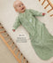 Happy baby lying in a wooden cot wearing a green long-sleeved sleeping bag with text overlay highlighting slim-fit design for an easy transition from swaddling.