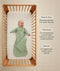 An overhead view of a baby wearing a long-sleeved, sage green leaf-patterned sleeping bag lying on their back inside a wooden cot. To the right, text details key features: wash & wear, TOG-rated, and Sleeved.