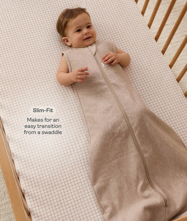 Infant lying in a wooden cot, wearing an ergoPouch Sleeping Bag  1.0 TOG Taupe Marle with text highlighting 