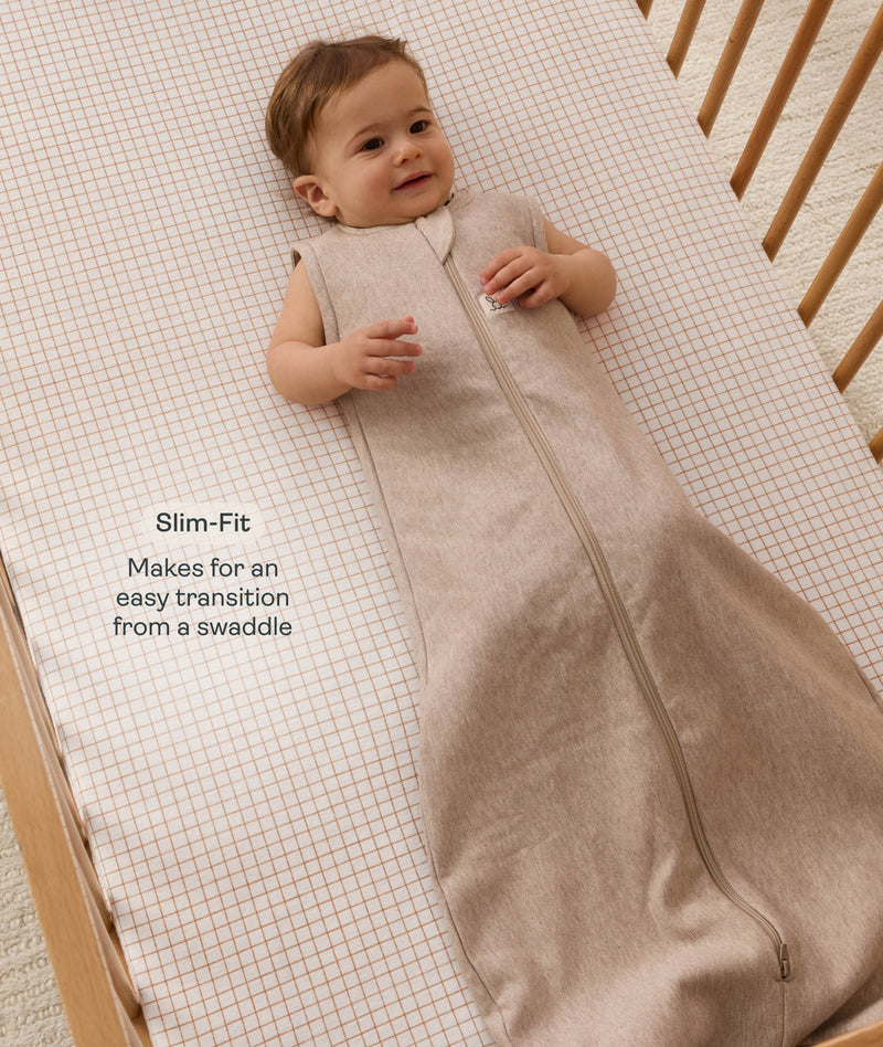 Infant lying in a wooden cot, wearing an ergoPouch Sleeping Bag  1.0 TOG Taupe Marle with text highlighting 