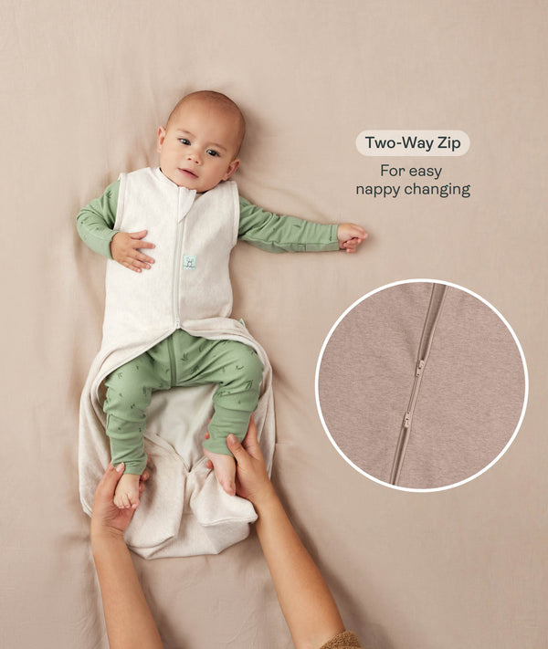 A baby lying down in a green long sleeve layer with an unzipped beige sleeping bag while adult hands hold their feet. Text highlighting 