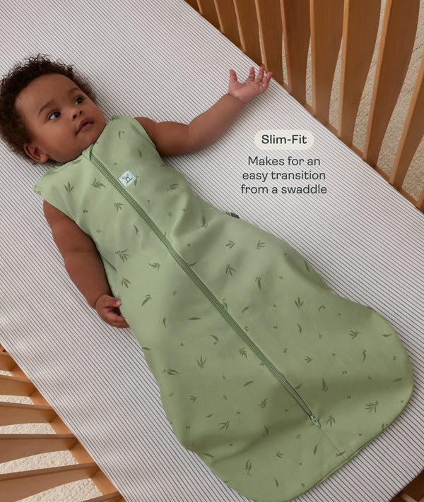 Infant lying in a wooden cot wearing sleeveless Sleeping Bag 1.0 TOG Willow with text highlighting slim-fit design for an easy transition from swaddling.
