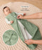 Baby lying on a padded mat while an adult adjusts the zipper of the baby's green sleeveless sleeping bag with text overlay highlighting two-way zip design for easy nappy changing.