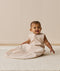 A smiling baby wearing a sleeveless Sleeping Bag 1.0 TOG, sitting upright on a white mat