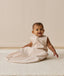 A smiling baby wearing a sleeveless Sleeping Bag 1.0 TOG, sitting upright on a white mat