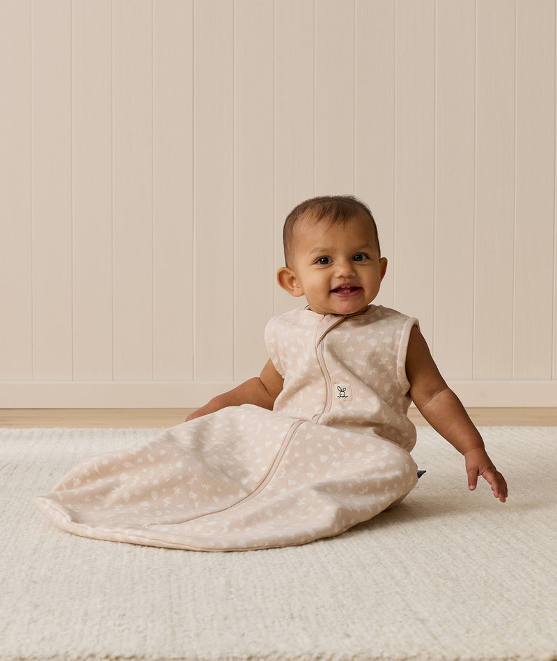 A smiling baby wearing a sleeveless Sleeping Bag 1.0 TOG, sitting upright on a white mat