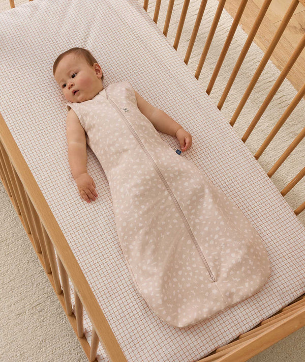 Infant wearing a sleeveless Sleeping Bag 1.0 TOG, lying inside a wooden cot with a grid-patterned sheet