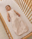 Infant wearing a sleeveless Sleeping Bag 1.0 TOG, lying inside a wooden cot with a grid-patterned sheet