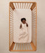 A smiling baby lying inside a wooden cot, wearing a sleeveless ergoPouch Sleeping Bag 1.0 TOG