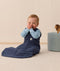 Baby sitting upright wearing a navy blue sleeping bag over a long sleeve layer.