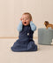Baby sitting upright wearing a navy blue sleeping bag, featuring a zip-front design and soft, breathable fabric.