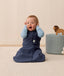 Baby sitting upright wearing a navy blue sleeping bag, featuring a zip-front design and soft, breathable fabric.