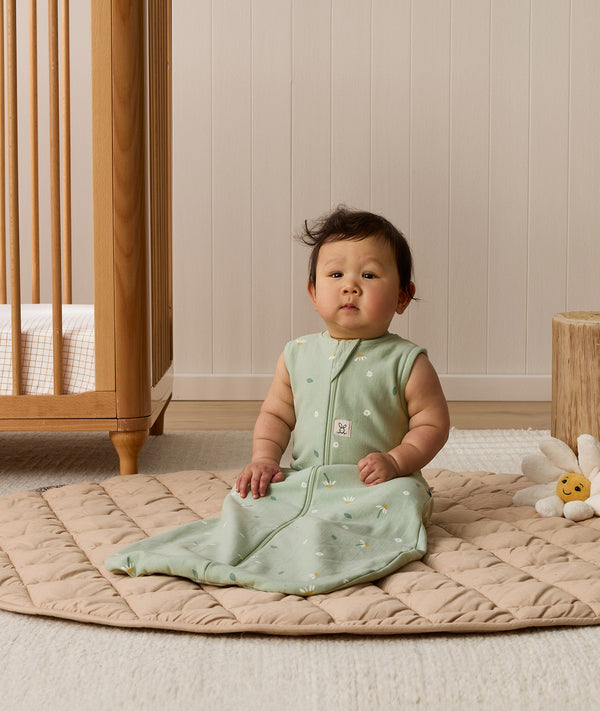 Infant sitting upright on a quilted mat, wearing a sleeveless sage green Sleeping Bag 1.0 TOG